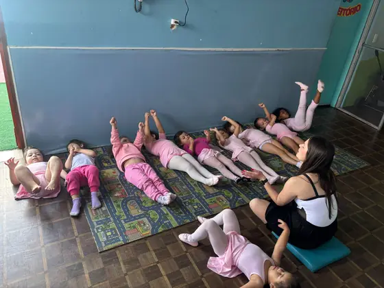 Exercício de perninhas no colchonete, com a professora orientando a turma
